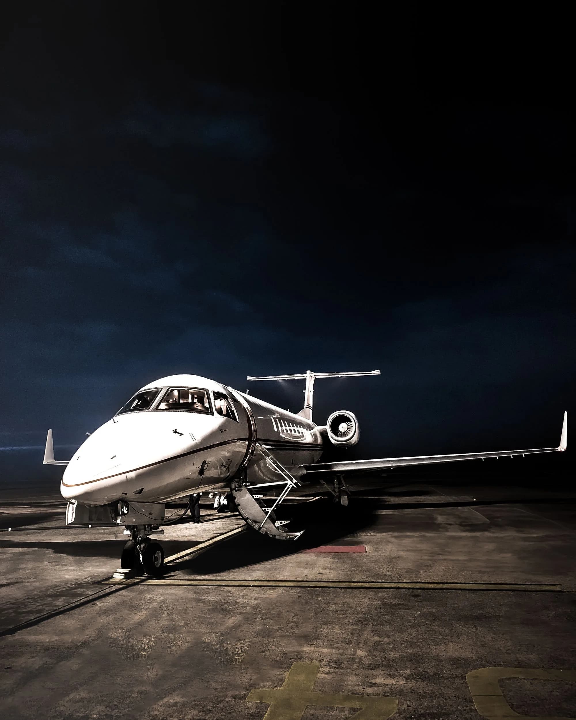 Executive private jet illuminated on an airport apron at night.