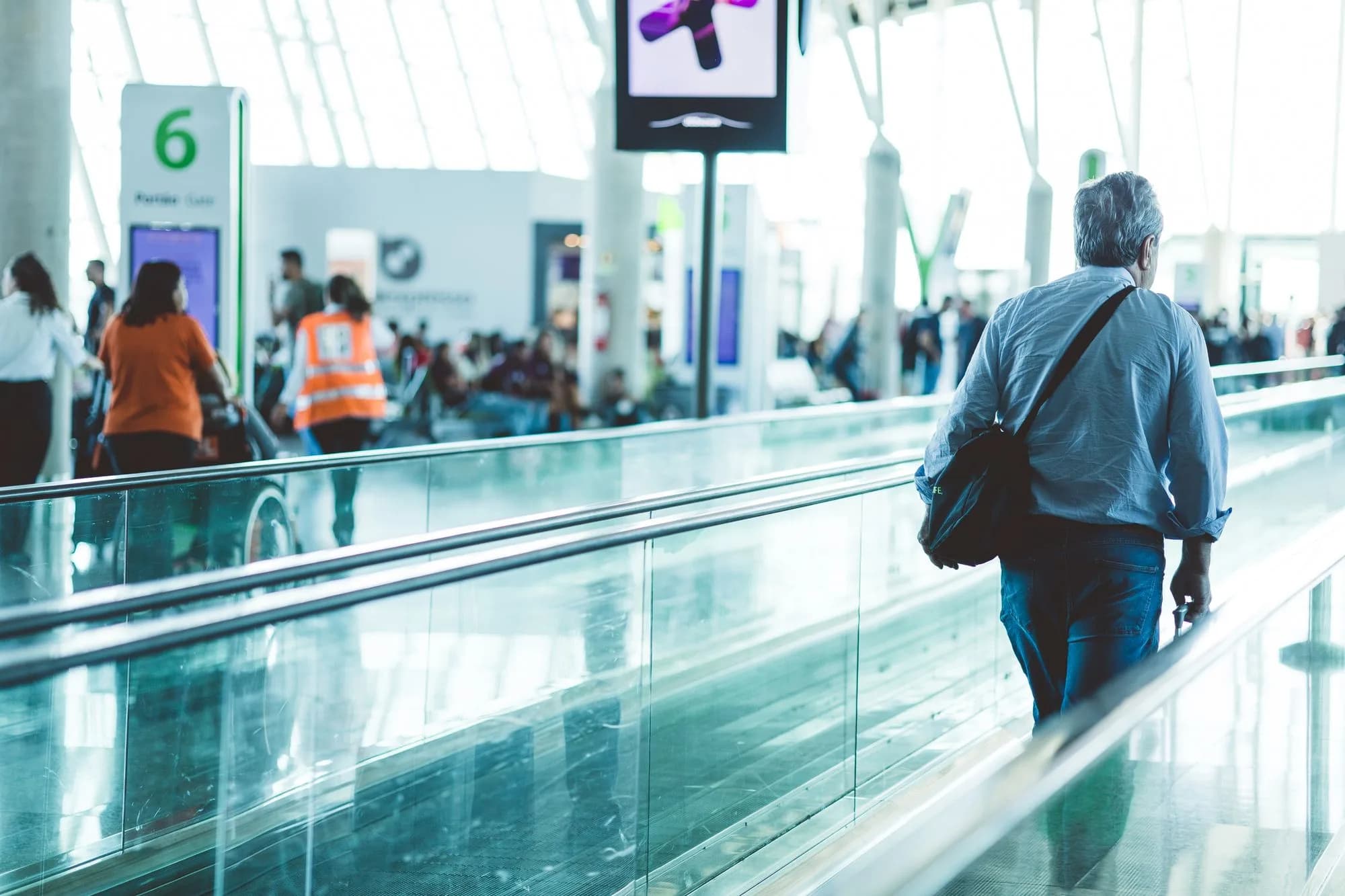International travellers moving through a bright modern airport concourse with luggage.