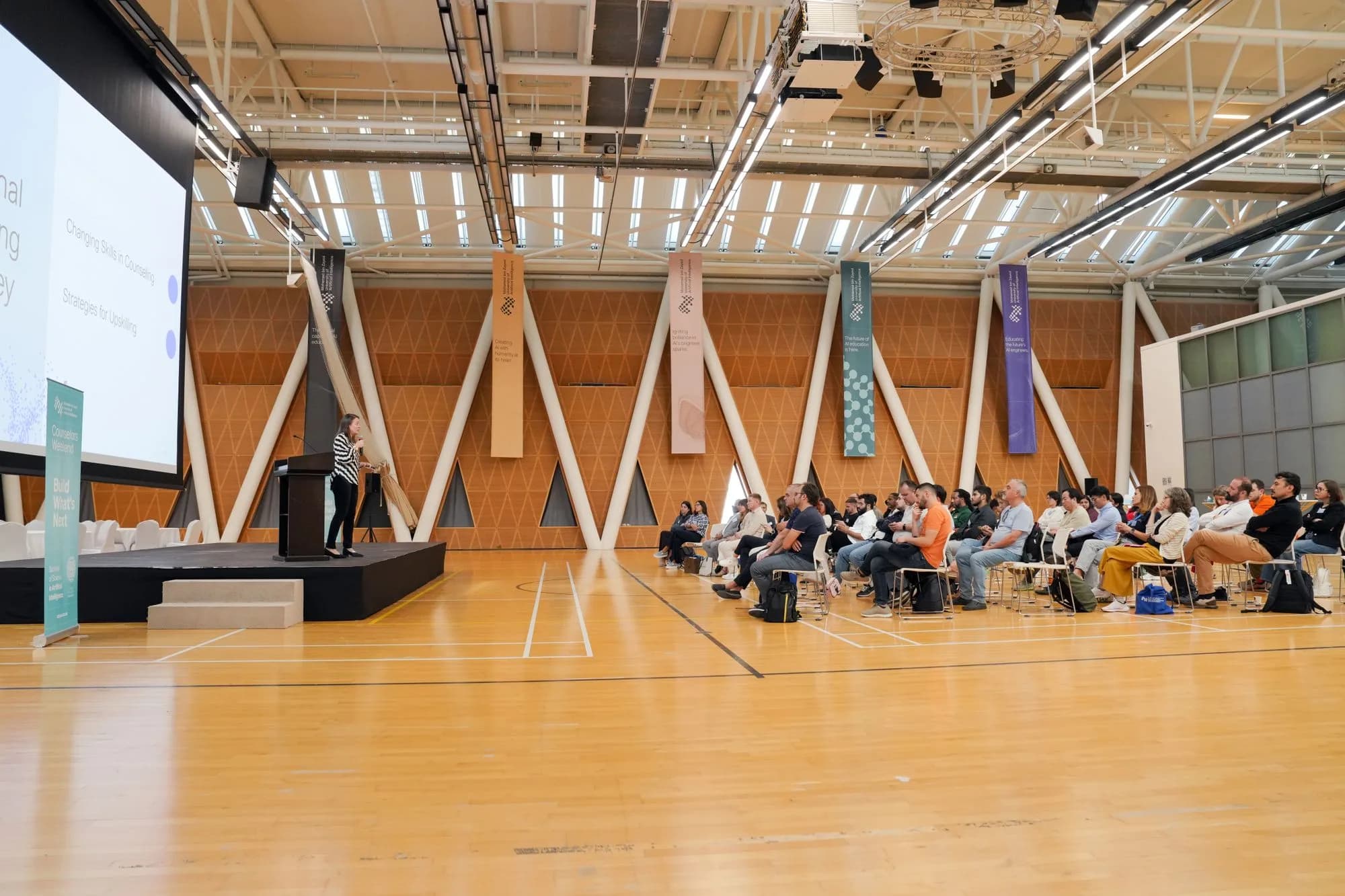 Professional audience listening to a speaker in a modern conference auditorium.