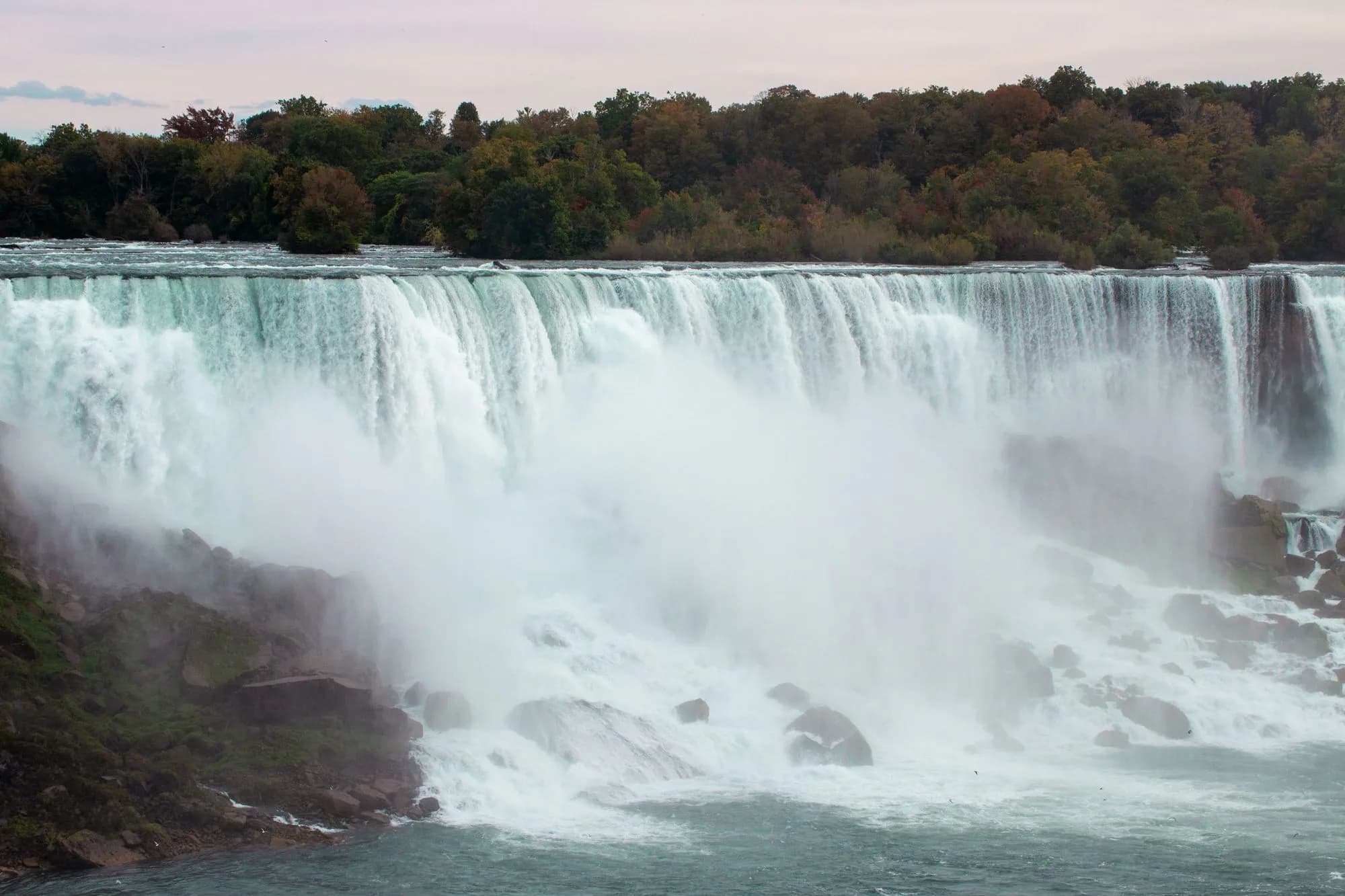 Niagara Falls surrounded by autumn foliage and rising mist on the Canadian side.
